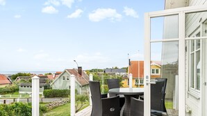 A wooden deck with a table and chairs, overlooking a residential area with houses and a clear sky. - Haveliden by Interhome (Hällevik)