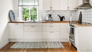 A modern kitchen with white cabinetry, a wooden countertop, a built-in oven, and a window with a view of greenery. - Haveliden by Interhome (Hällevik)