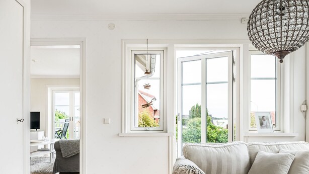 A modern living room with a sofa, a coffee table, and a large window with a view of greenery and a building. - Haveliden by Interhome (Hällevik)