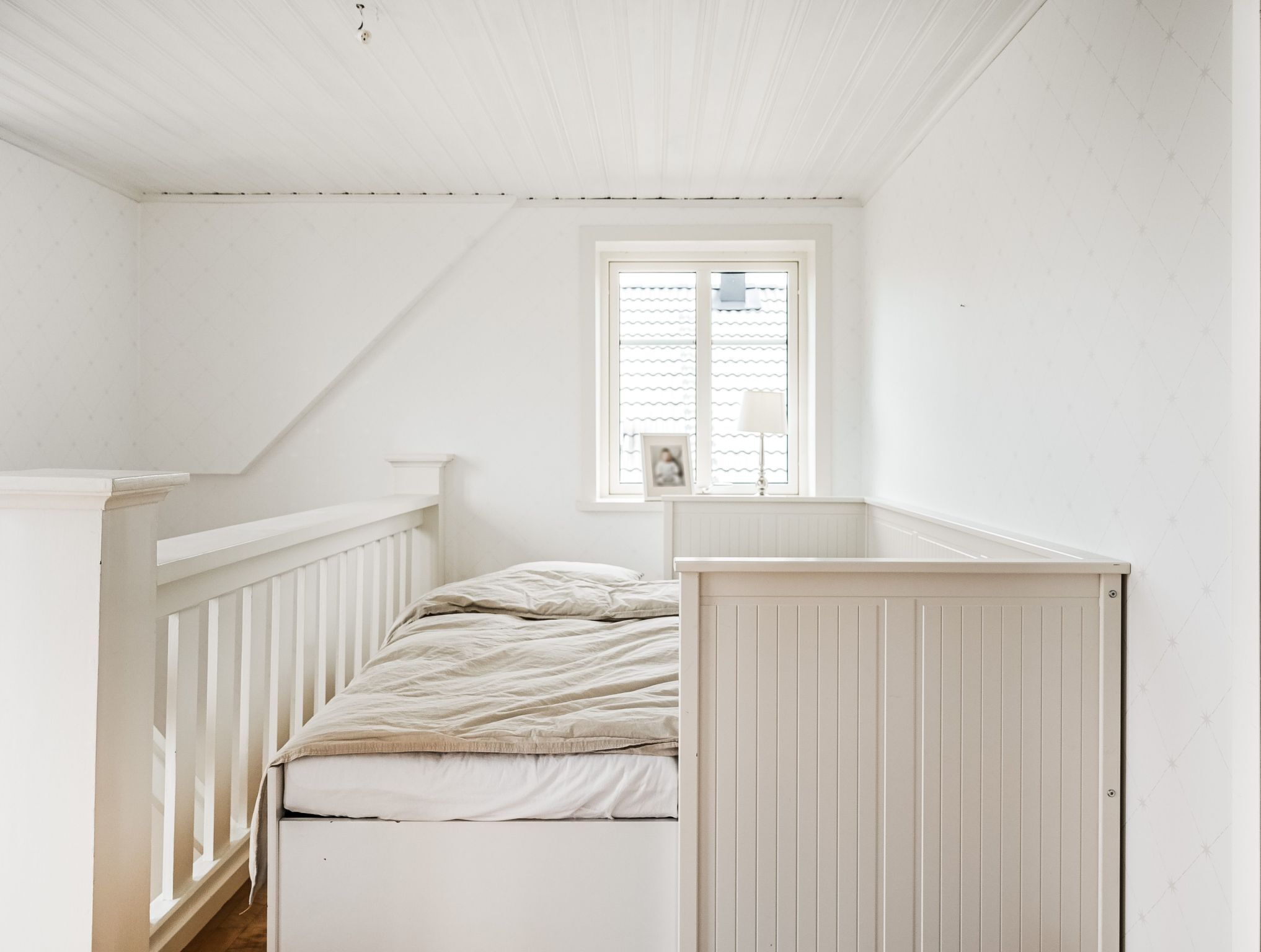 A small, white room with a single bed, a window with blinds, and a white radiator.