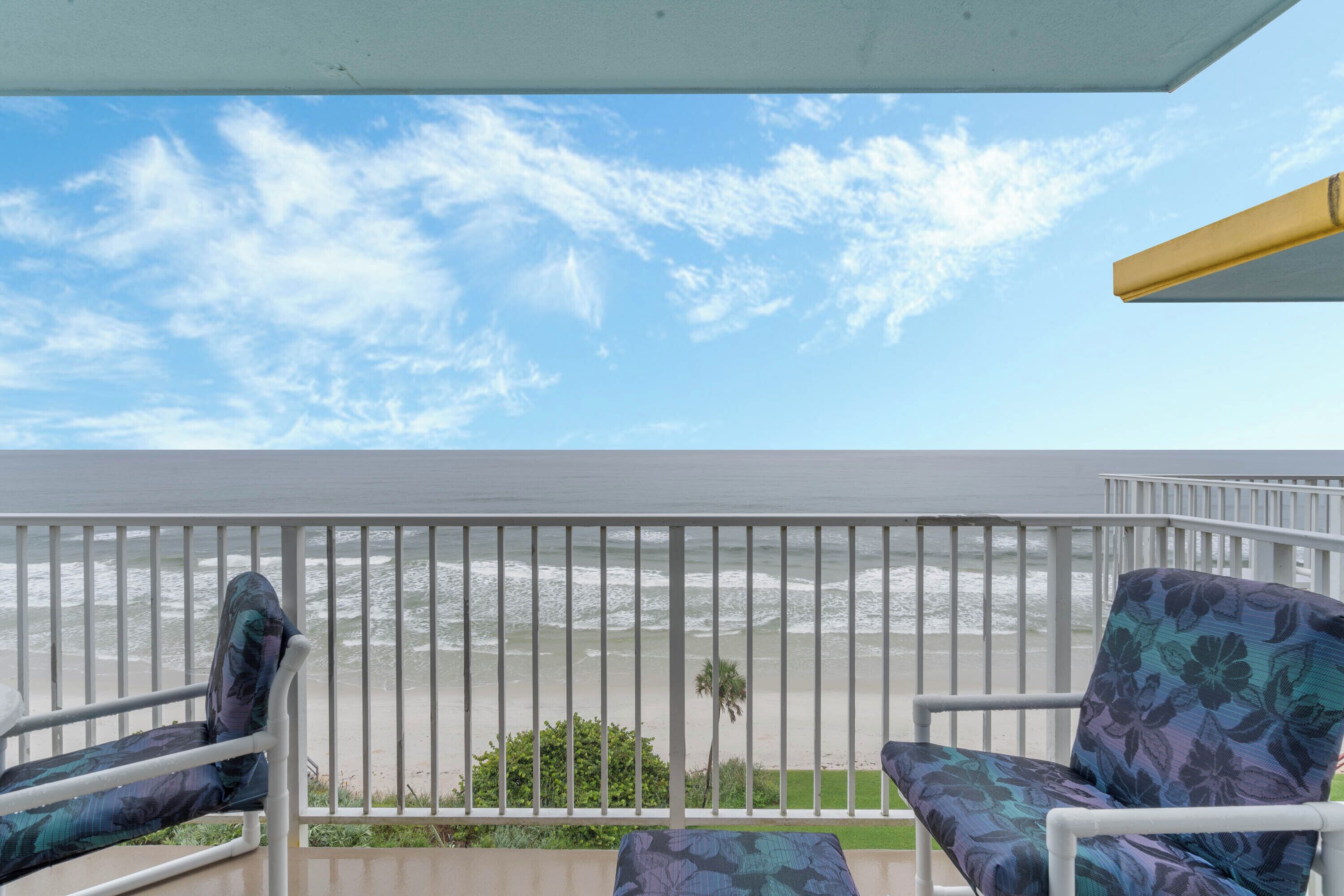 A balcony with two chairs, a railing, and a view of the beach.