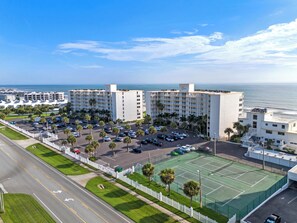A hotel with multiple floors, a parking lot, and a tennis court.