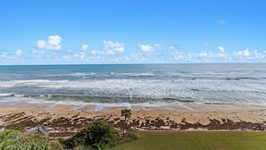 Uma praia com ondas, céu claro e horizonte distante.