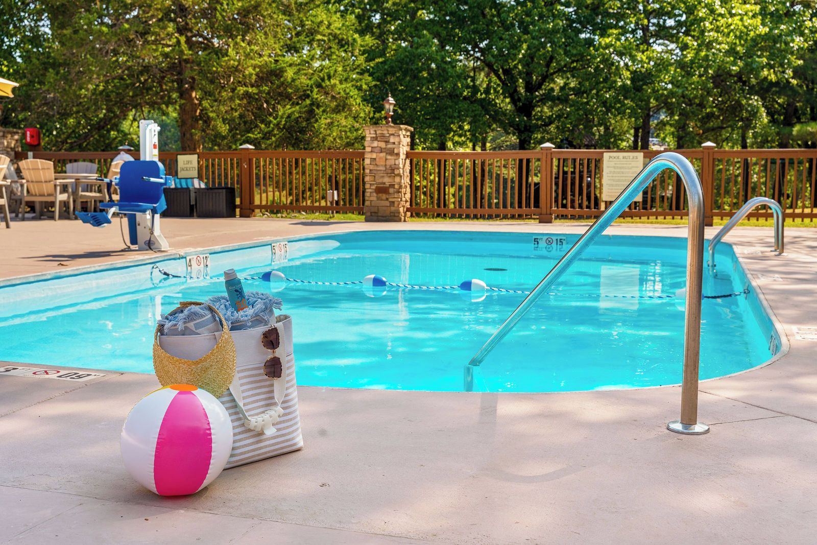 Una piscina con una silla de salvavidas, una escalera de piscina y una pelota de playa.
