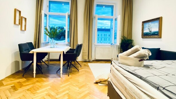 Una habitación con una cama, una mesa con sillas, una ventana con cortinas y un cuadro en la pared.