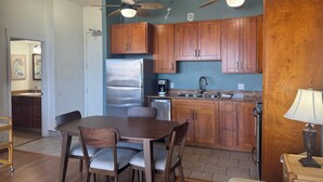 Une cuisine avec des meubles en bois, un réfrigérateur en acier inoxydable, une table à manger avec des chaises et des ventilateurs de plafond.