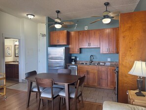 Una cocina con armarios de madera, un refrigerador de acero inoxidable, una mesa de comedor con sillas y ventiladores de techo.