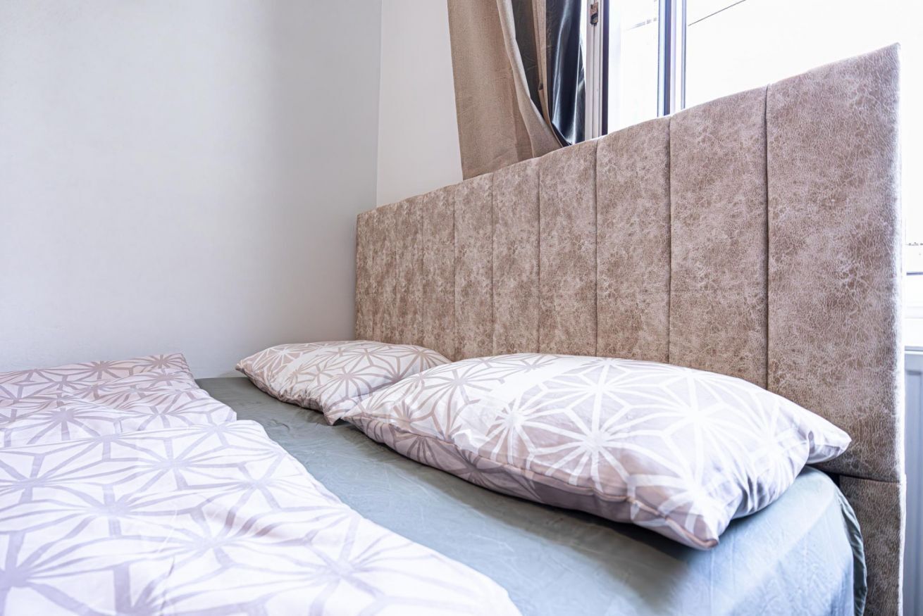 Ein Bett mit Kopfteil, zwei Kissen und einer gemusterten Tagesdecke.