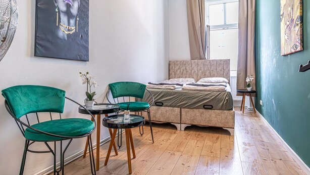 A bedroom with a bed, two chairs, a small table, a window with curtains, and artwork on the walls. - Chic Cozy Studio, 15 min to City Center (Vienna)