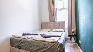 Ein Schlafzimmer mit einem Bett, einem Fenster mit Vorhängen, einem kleinen Tisch mit Pflanze und einer grünen Wand.