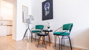A room with a wooden floor, a tripod fan, two green chairs, a small round table, and a black and white artwork on the wall. - Chic Cozy Studio, 15 min to City Center (Vienna)