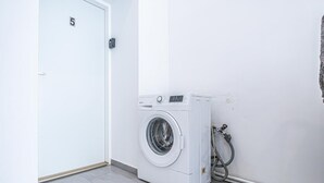 A laundry room with a washing machine, a door marked with the number 5, and a hose connected to the wall. - Chic Cozy Studio, 15 min to City Center (Vienna)
