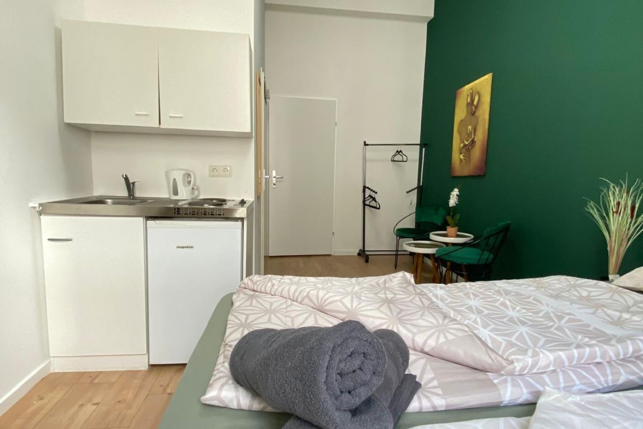 Een compacte kamer met een bed, een klein kitchenette, een groene wand en een deur naar een andere kamer.