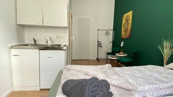 Een compacte kamer met een bed, een klein kitchenette, een groene wand en een deur naar een andere kamer.