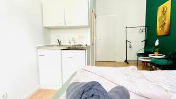 Ein Schlafzimmer mit Bett, gerolltem Handtuch, einer kleinen Küchenzeile und einer grünen Wand mit einem Gemälde.