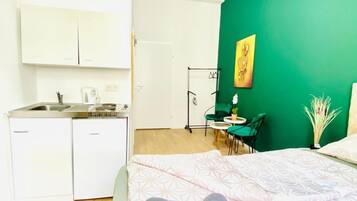 A compact room with a kitchenette, a bed with a patterned bedspread, a green accent wall, and a small dining area.