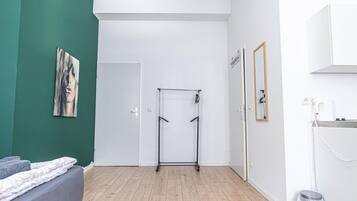 Ein Zimmer mit einem Bett, einer Tür, einem Metallregal, einem Spiegel und einer Mülleimer.