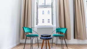 Ein Zimmer mit Fenster, zwei Stühlen, einem kleinen Tisch und einer Heizung.