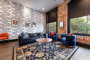 Una sala de estar moderna con una pared de ladrillo, un ventanal grande, un sofá de cuero negro, sillones azules, un tapete estampado y una pequeña mesa redonda.