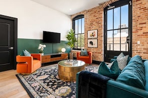 A modern living room with a brick wall, a flat-screen TV, a round coffee table, and a teal sofa.