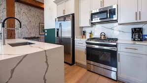 A modern kitchen with white cabinets, stainless steel appliances, and a marble countertop. - King Suite & Private Terrace Walk Everywhere Hotel (New Orleans)