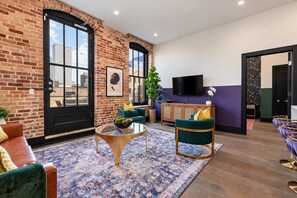 Ein modernes Wohnzimmer mit Backsteinwand, großem Fenster, Flachbildfernseher und einem grünen Sofa.