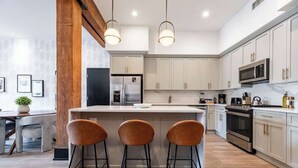 Cozinha moderna com ilha central, banquetas, eletrodomésticos de aço inoxidável e armários em tons claros.