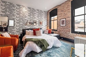 Une chambre d’hôtel avec un mur en briques, un grand lit, des meubles orange et blancs, et une fenêtre donnant sur un paysage agréable.