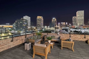 A rooftop terrace with outdoor furniture, a brick wall, and a city skyline view at night. - Spacious Downtown Suite w/Sleeper Sofa Hotel (New Orleans)