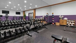 Un gimnasio con equipamiento de levantamiento de pesas, bancos y un espejo grande.