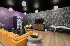 Ein modernes Wohnzimmer mit einer violetten Wand, einem gelben Sofa, einem Couchtisch mit einer Schale, einem Fernseher und einem Verkaufsautomaten.