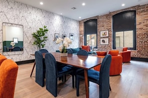 A modern interior with a wooden dining table, blue chairs, orange sofas, and a brick wall. - Prime Location Downtown Hotel (New Orleans)