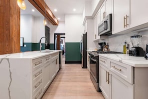 A modern kitchen with white cabinets, stainless steel appliances, and a wooden accent wall. - Prime Location Downtown Hotel (New Orleans)