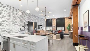 Une cuisine moderne dotée d’un îlot en marbre, de luminaires suspendus et d’un mur en briques orné d’inscriptions.