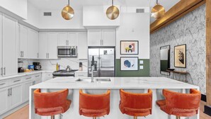 Una cocina moderna con armarios blancos, electrodomésticos de acero inoxidable y una isla central con taburetes de bar.