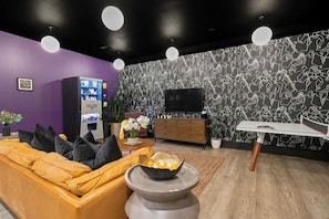 A modern living room with a purple wall, a yellow sofa, a coffee table with a bowl, a TV, and a vending machine. - Downtown NOLA Luxury Suite Hotel Rooftop Pool Sleeps 6 (New Orleans)