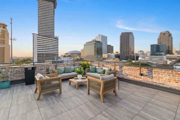 Una terraza en la azotea con mobiliario exterior, un muro de ladrillo y el horizonte de la ciudad al fondo.