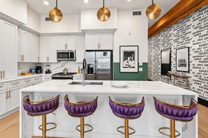 Una cocina moderna con armarios blancos, electrodomésticos de acero inoxidable y una isla central con taburetes de bar.