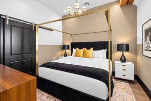A four-poster bed with a black and white bedspread, two bedside lamps, and a white nightstand with drawers. - Spa Suite Bath Rooftop Pool BBQ Gym Hotel (New Orleans)