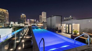 Uma piscina no terraço com vista para o horizonte da cidade, um edifício moderno com fachada de vidro e céu claro.