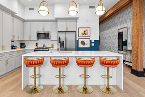 Cocina moderna con armarios blancos, electrodomésticos de acero inoxidable y una isla central con taburetes de bar.