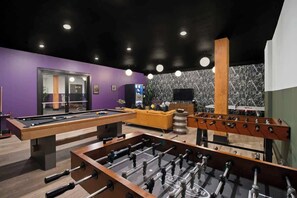 A billiards table, a foosball table, and a pool table in a room with purple walls and a marble-patterned wall.