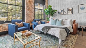 Ein Zimmer mit großem Fenster, roter Backsteinwand, Bett, blauem Sofa und Couchtisch.