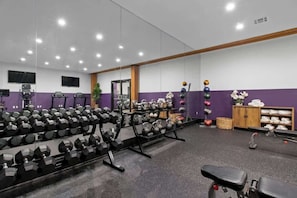 A gym with weightlifting equipment, benches, and a mirrored wall.
