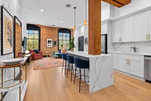 A modern kitchen with a marble countertop, a bar area with stools, and a brick wall.