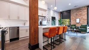 A modern kitchen with white cabinets, a wooden column, and a bar area with orange chairs. - Lux 2BR Suite Near Dome and FQ Hotel (New Orleans)