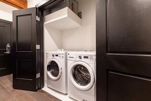 A laundry room with two front-loading washing machines, a dark wooden door, and a white ceiling.
