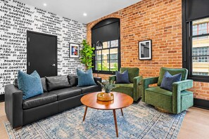 A modern living room with a brick wall, black and white patterned wallpaper, leather sofa, green armchairs, and a coffee table.