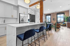 A modern kitchen with a marble countertop, stainless steel appliances, and a brick wall.