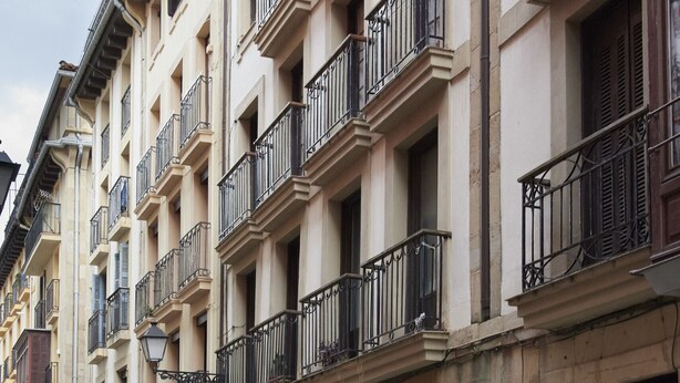 Eine Reihe mehrstöckiger Gebäude mit Balkonen, eine Straße davor und ein Geschäft mit einer Schaufensterschild.